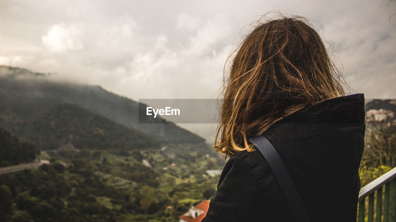 Rear view of woman standing at observation point against cloudy sky