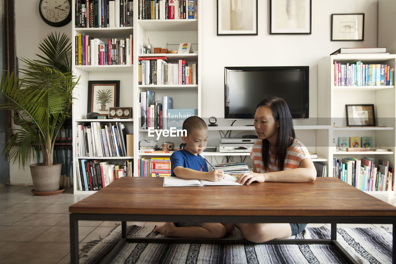 Mother assisting son in doing homework while sitting at home