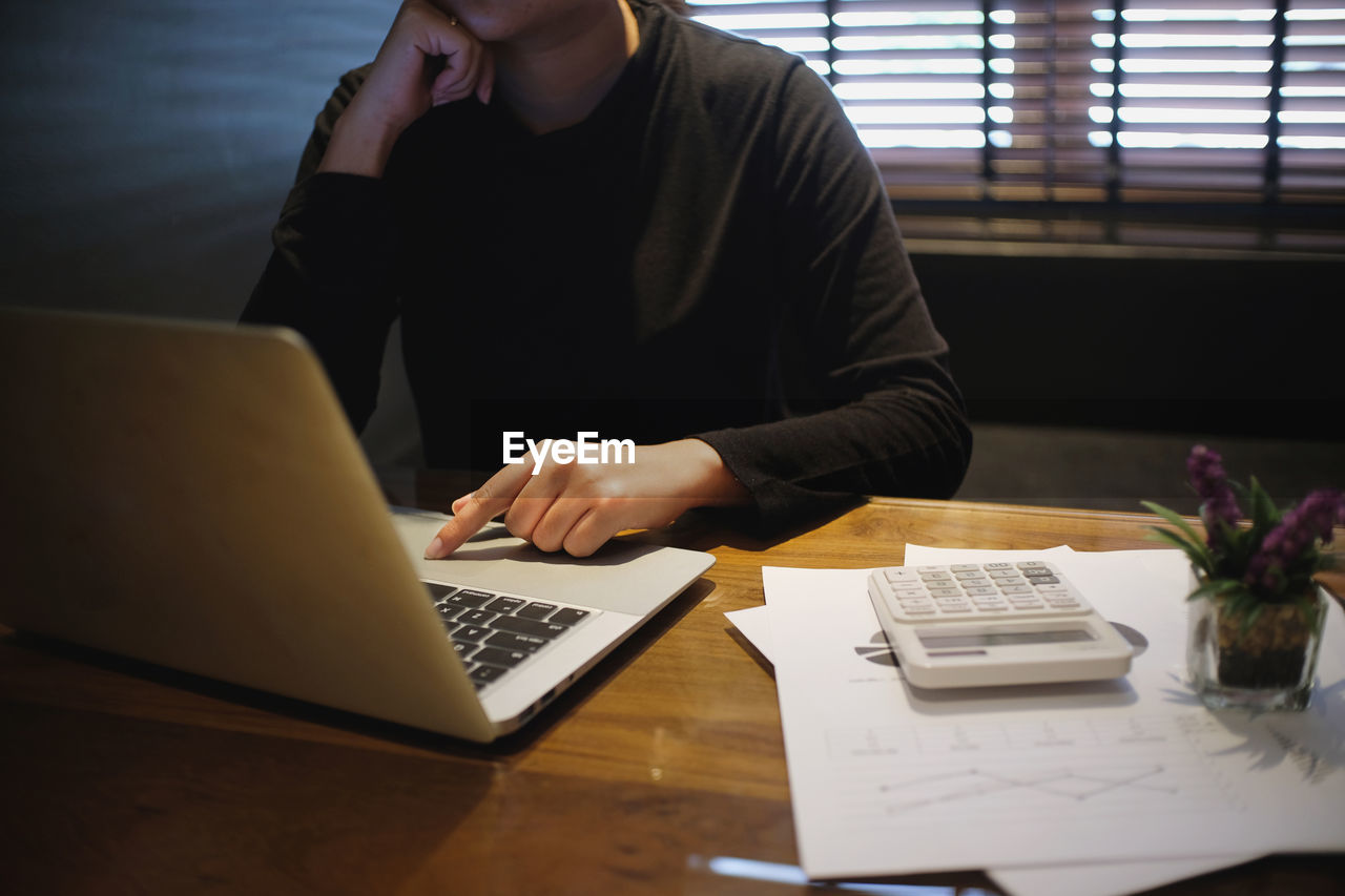 Midsection of businesswoman using laptop at desk in office