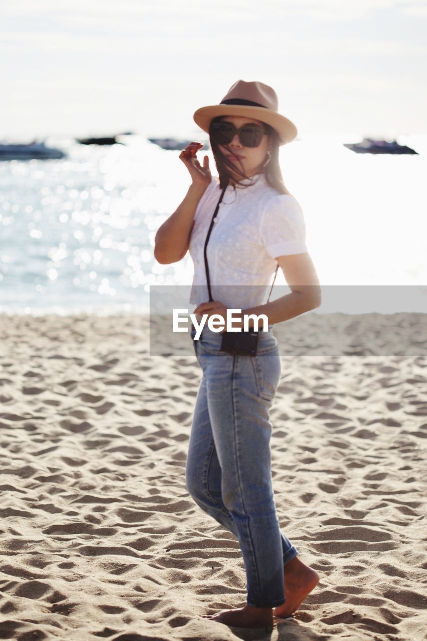 Portrait of woman wearing sunglasses while standing at beach