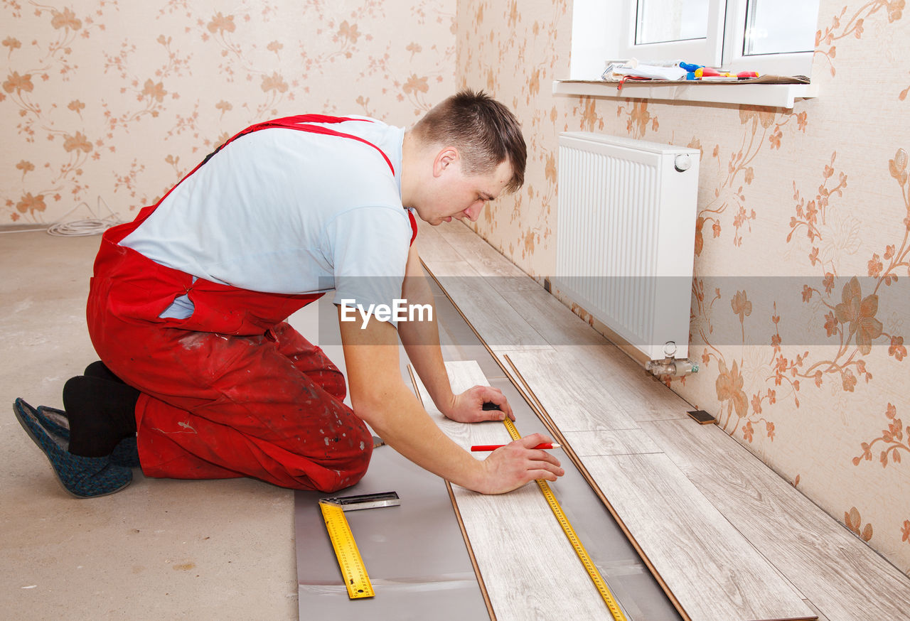 Man measuring hardwood floor panels in home