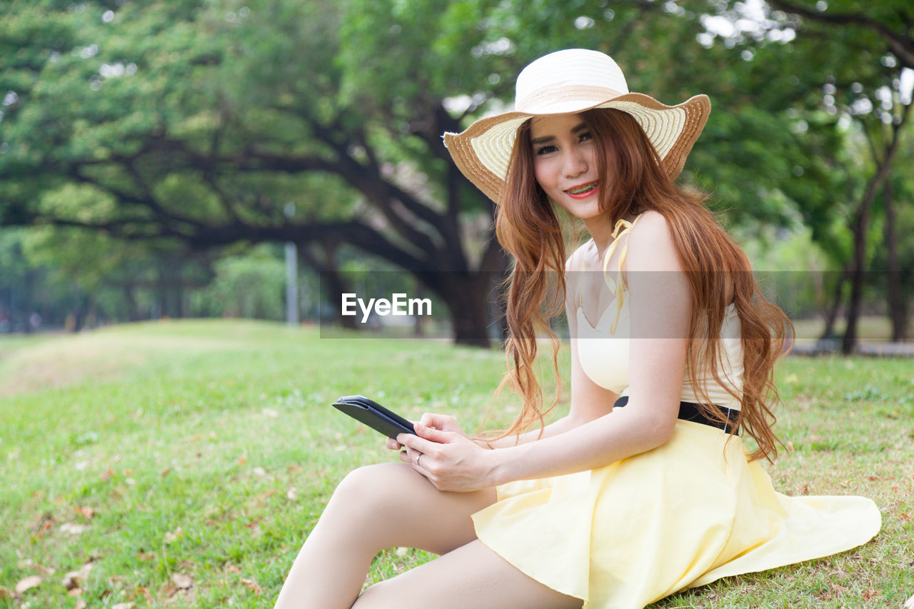 Close-up of young woman holding digital tablet while sitting on grass field