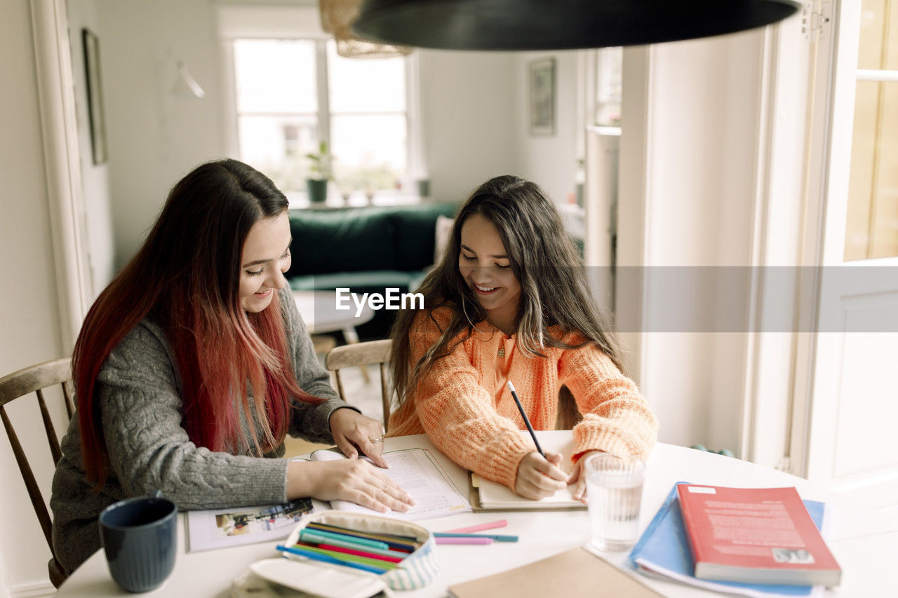 Happy woman assisting daughter in homework while sitting at table