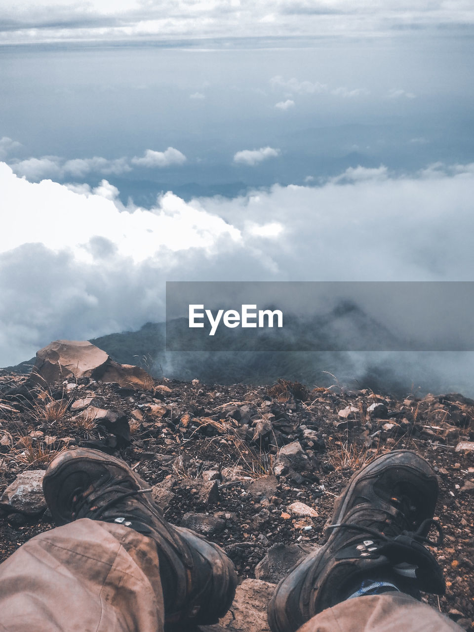 Low section of man sitting on mountain against sky