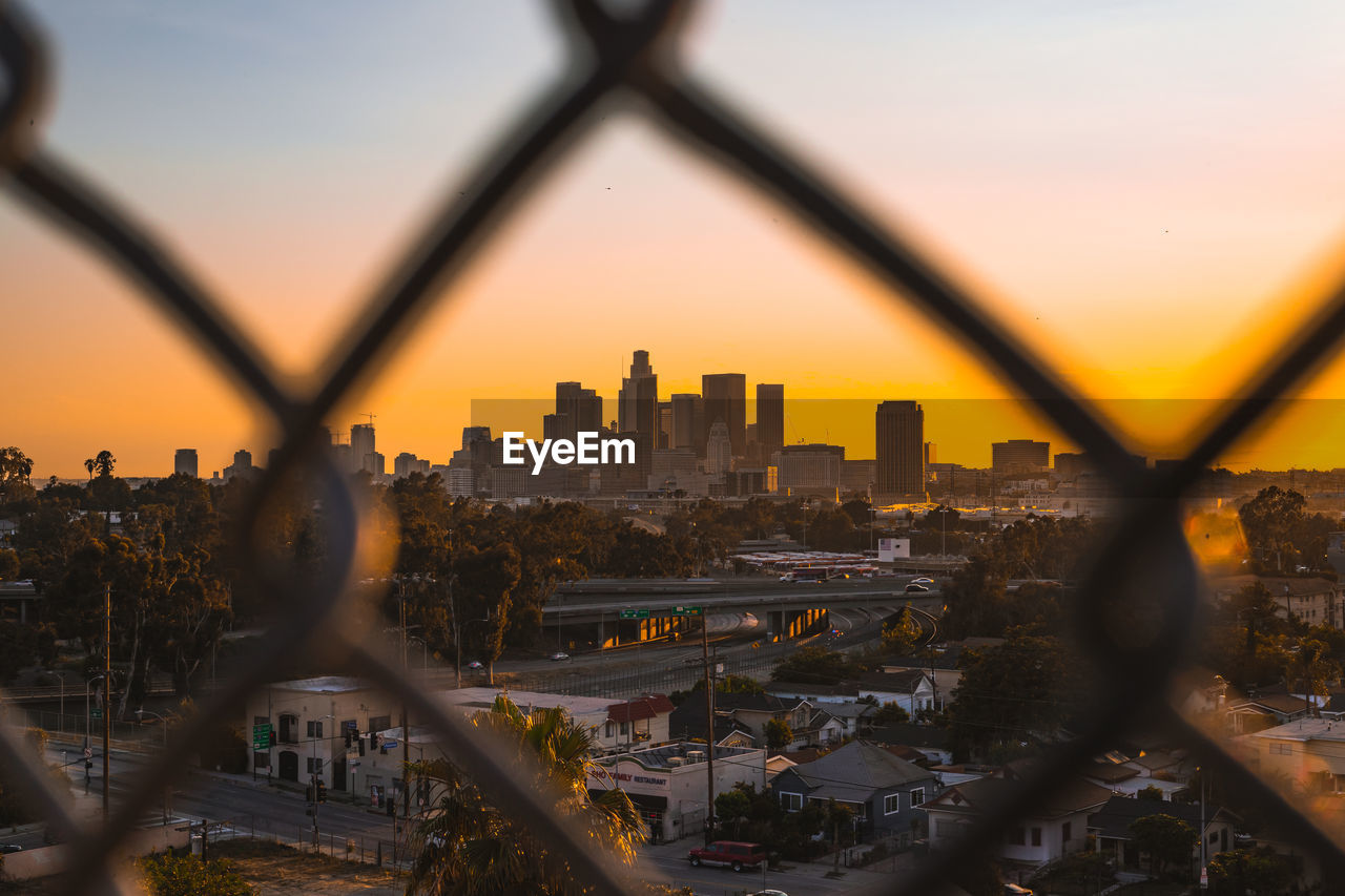 Los angeles cityscape seen through chainlink fence during sunset