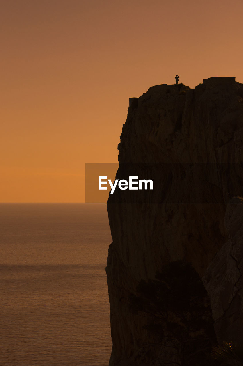 Silhouette cliff by sea against sky during sunset