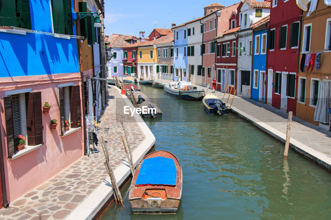 Boats moored on canal by colorful buildings at burano island