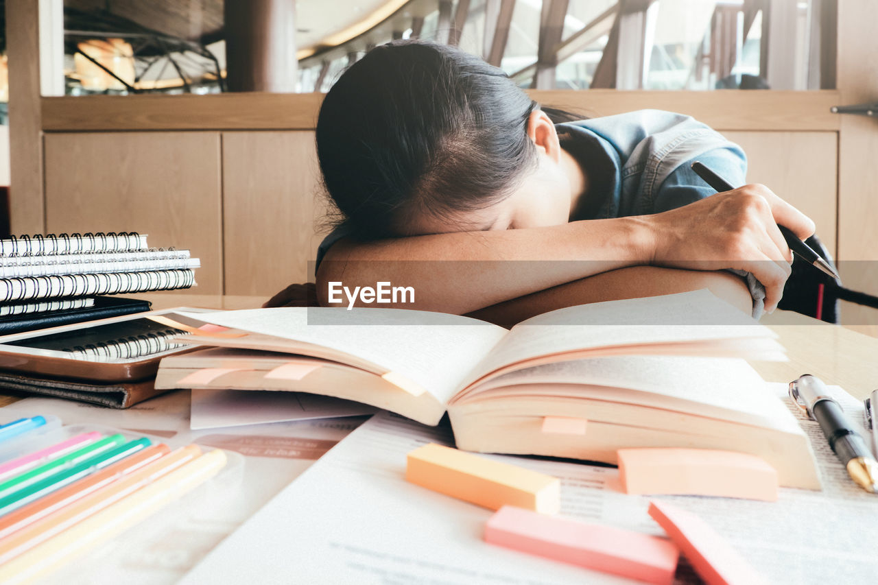 Close-up of woman sleeping by books at table