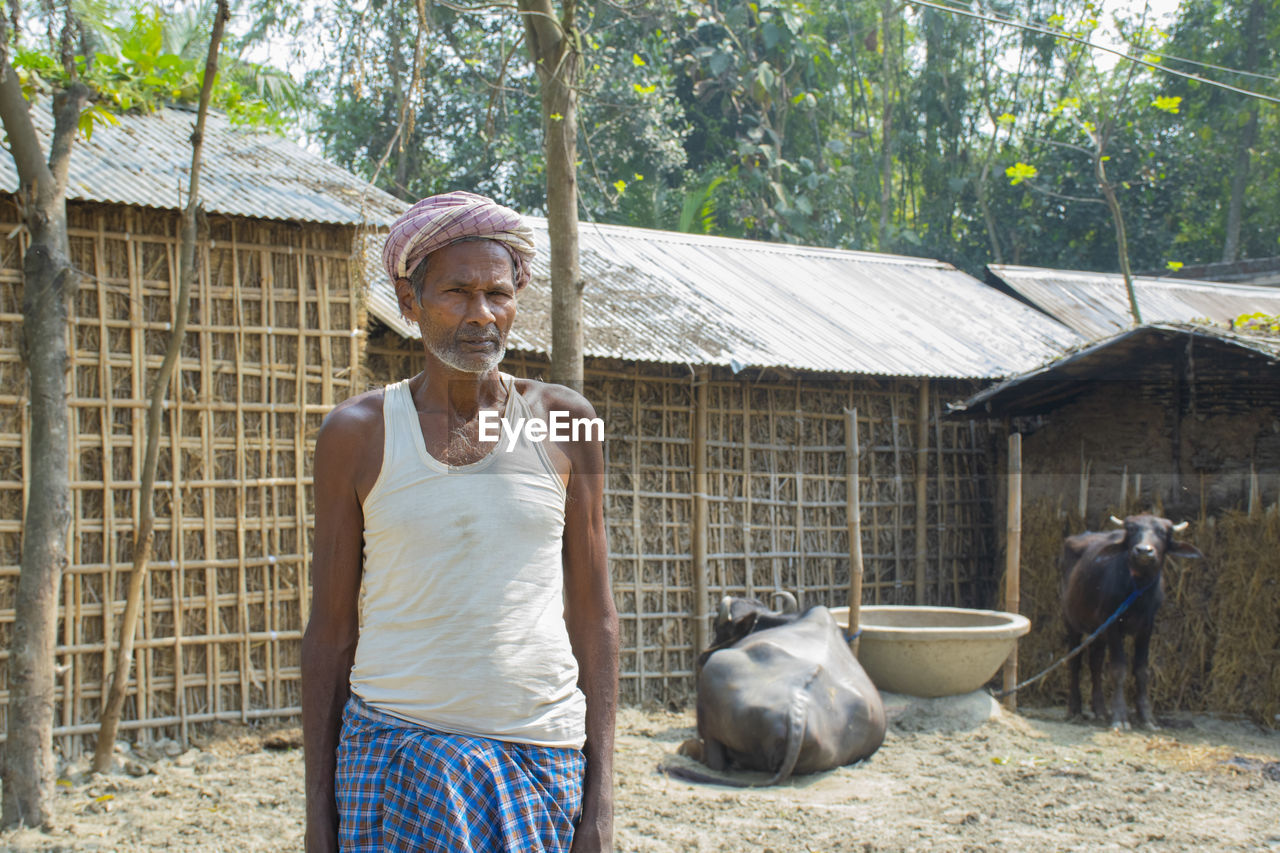 Indian farmer standing in front of his cattle and kacha house