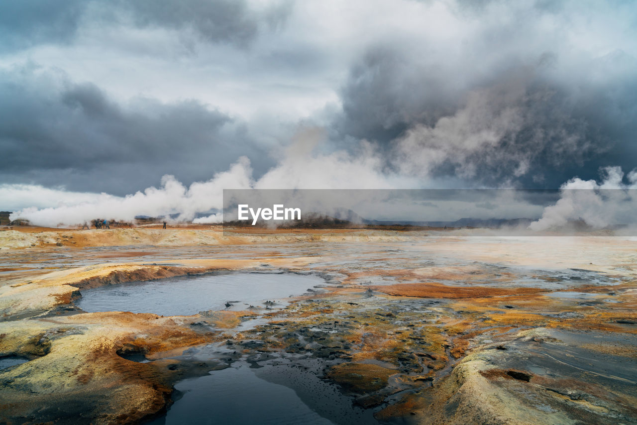 Scenic view of steam emitting from hot spring amidst landscape against cloudy sky