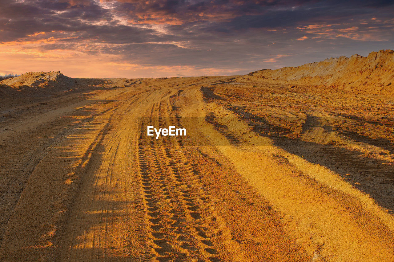 landscape, environment, land, sky, scenics - nature, nature, natural environment, desert, horizon, sand, beauty in nature, cloud, soil, road, sunset, sunlight, travel, no people, travel destinations, field, sun, outdoors, transportation, tranquility, hill, arid climate, horizon over land, sand dune, climate, dramatic sky, prairie, dusk, plain, non-urban scene, dry, urban skyline, the way forward, yellow, tourism, plateau, dirt, tranquil scene, remote, agriculture, semi-arid, orange color, day