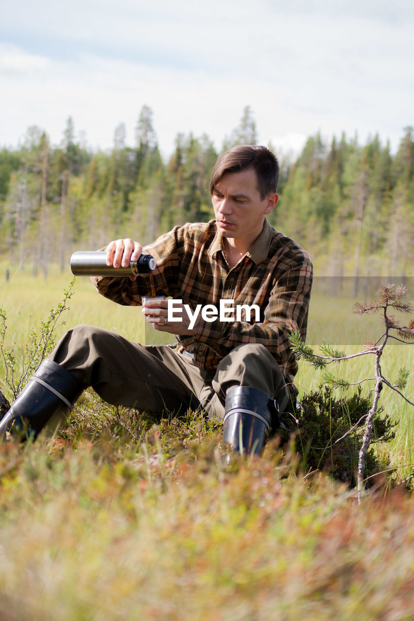 Man pouring coffee from bottle on grassy field against sky