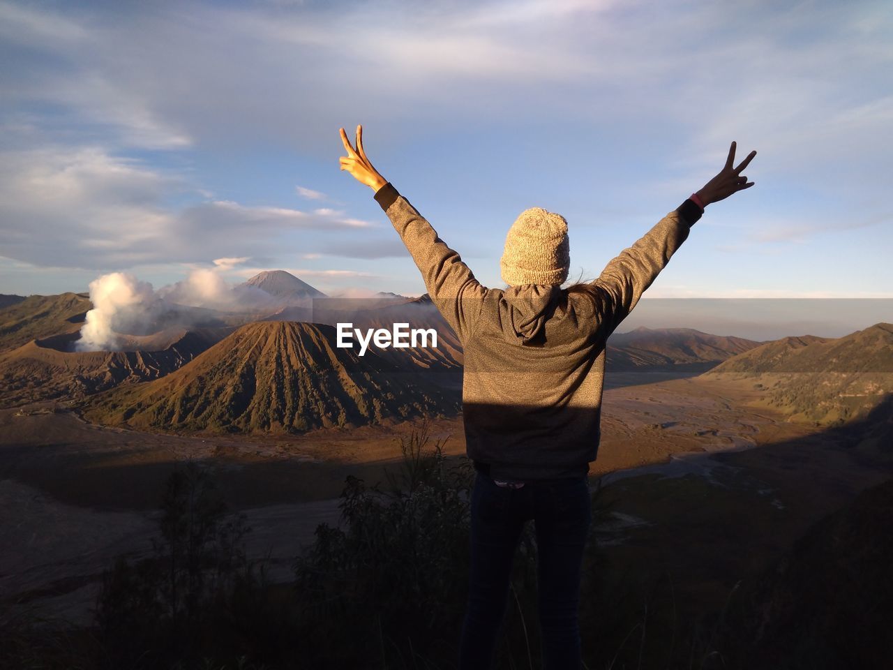 Woman standing on top of cliff at sunrise and enjoying view of bromo mountain 