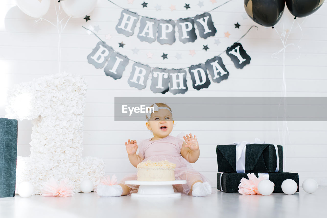 A one year old girl sits on the floor near a sweet cake in honor of her first birthday, tries 