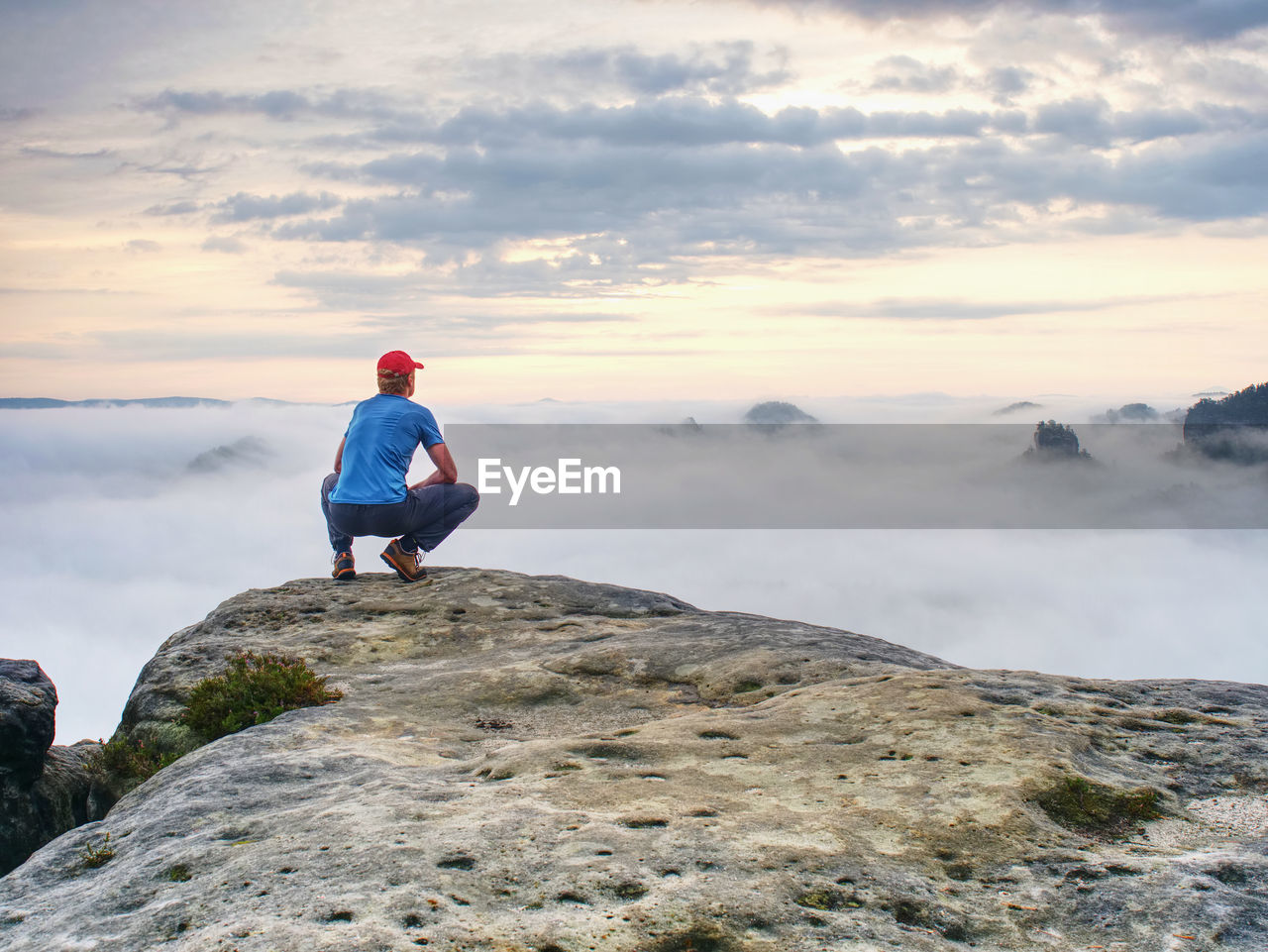 Hiker in middle of nowhere and thinking alone. man sit on top of a sharp peak enjoying sunrise.