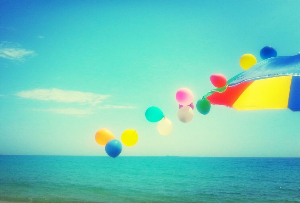 Cropped image of parasol with colorful balloons over sea against sky
