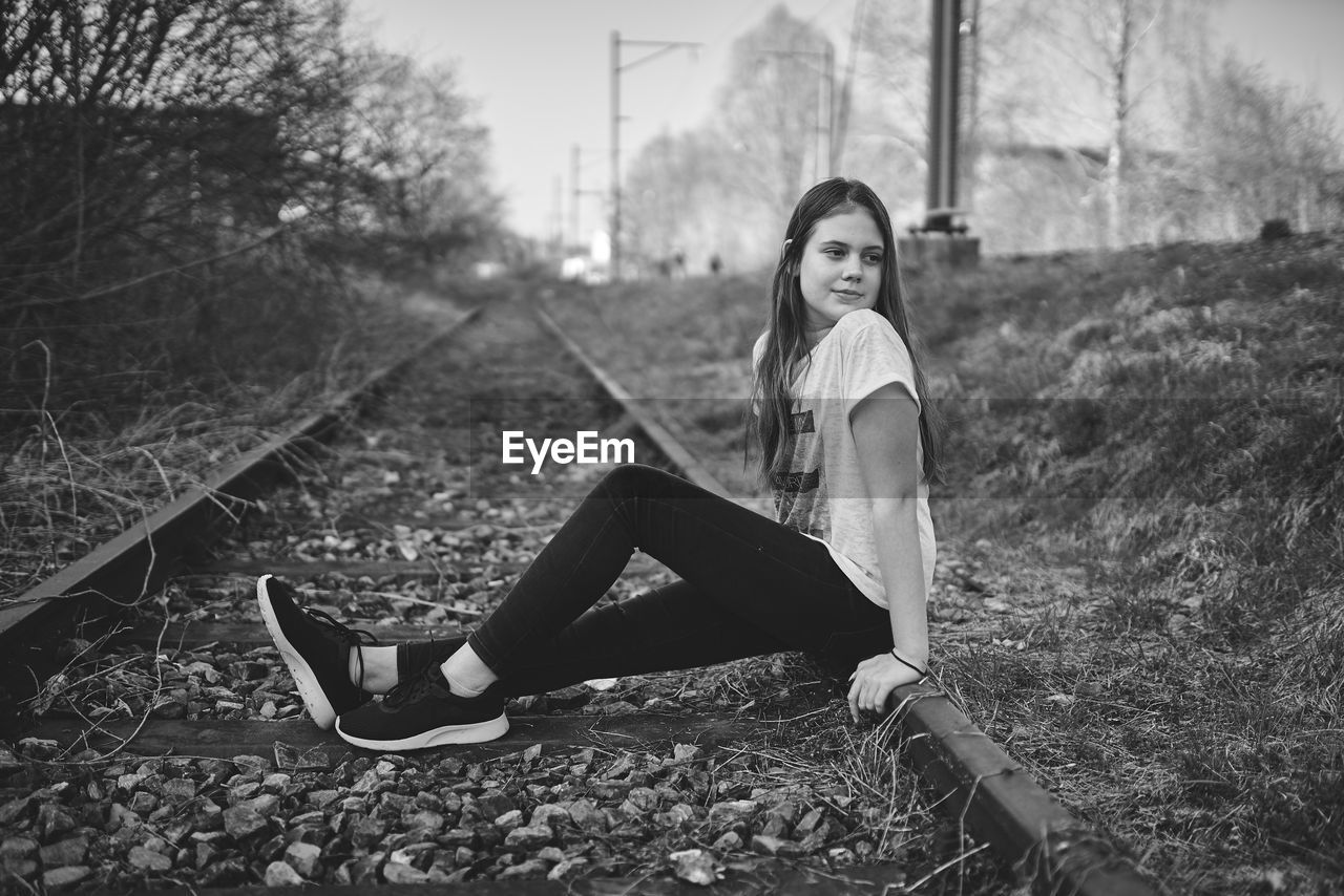 Side view of thoughtful girl sitting on railroad track