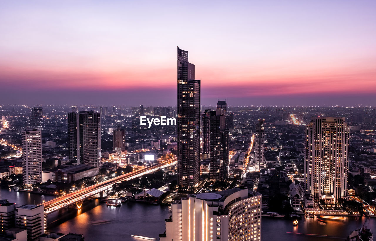 Illuminated buildings in city against sky at sunset