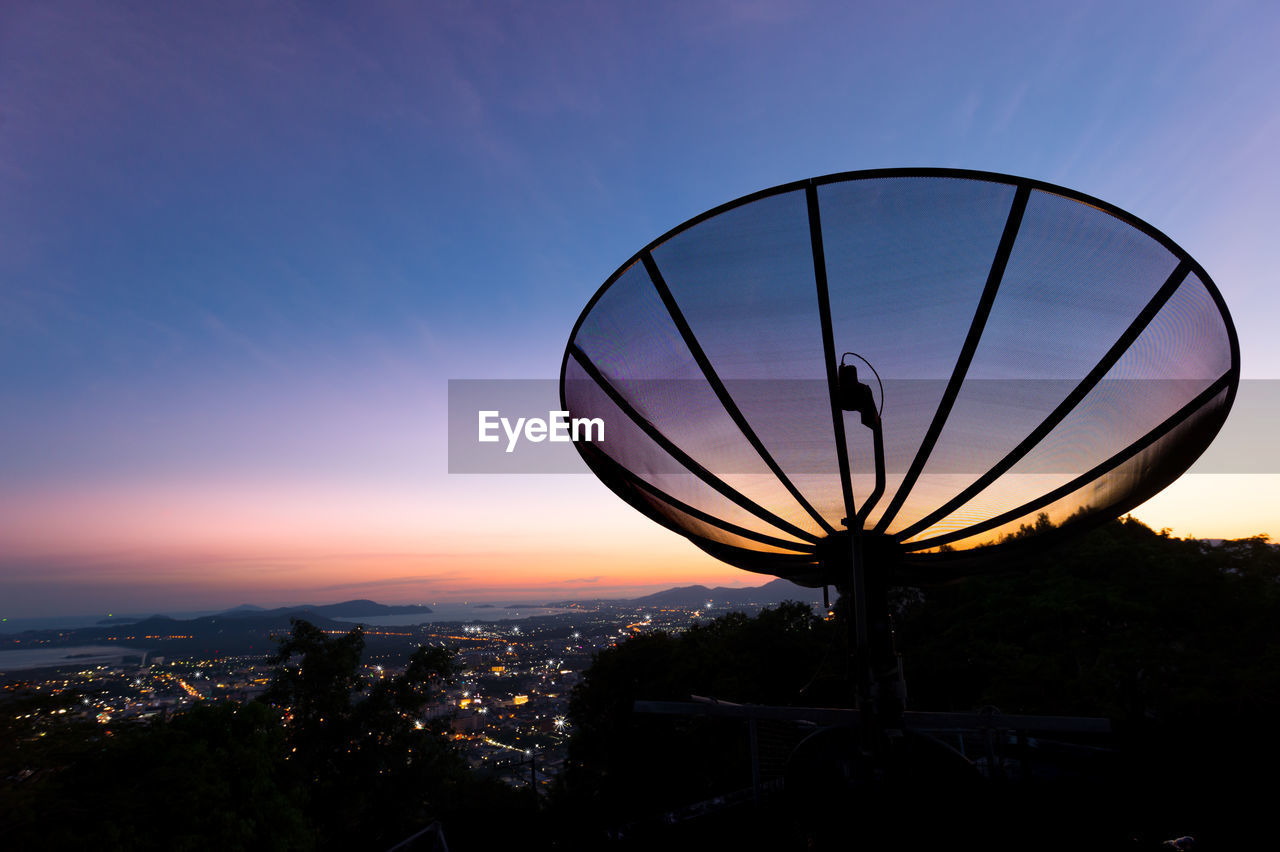Silhouette communications tower and cityscape against sky during sunset