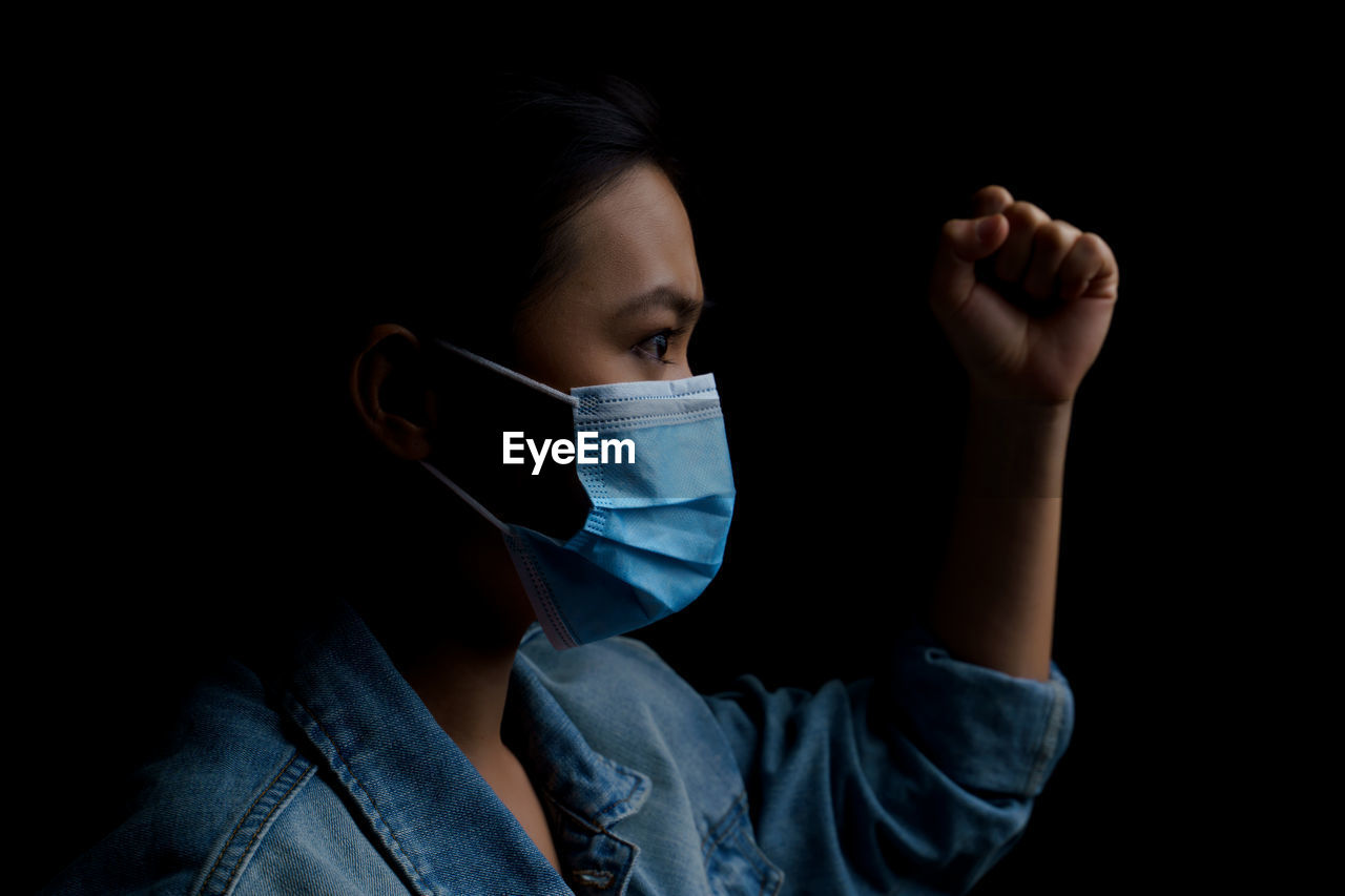 Close-up of young woman wearing flu mask standing against black background