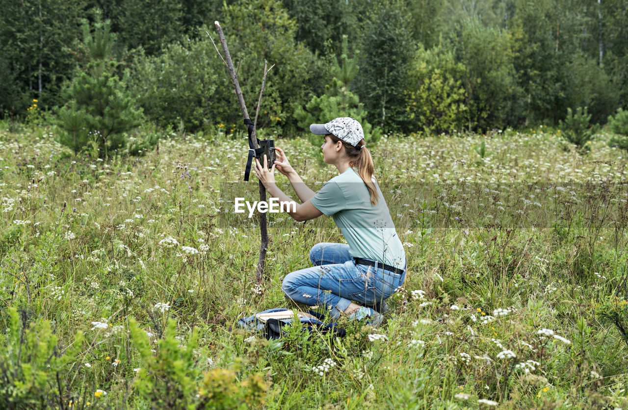 Young woman zoologist sets camera trap for observing wild rare animals to collect scientific data 