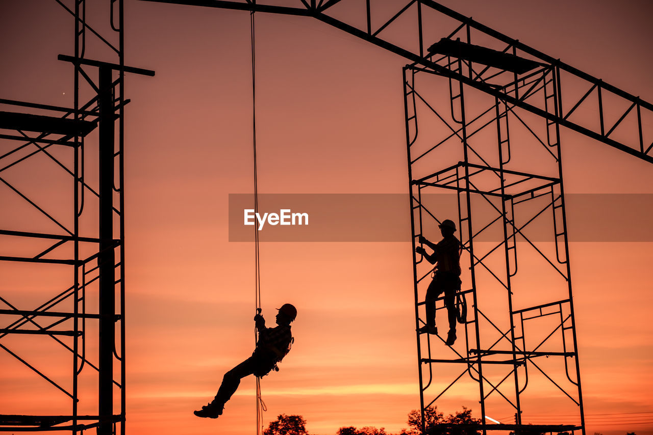 Low angle view of worker working on construction site against sky during sunset