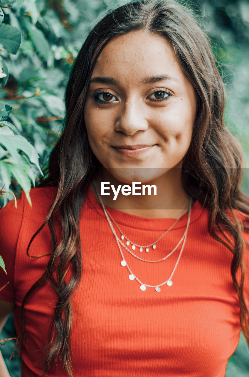 Portrait of a smiling young woman standing by plants outdoors