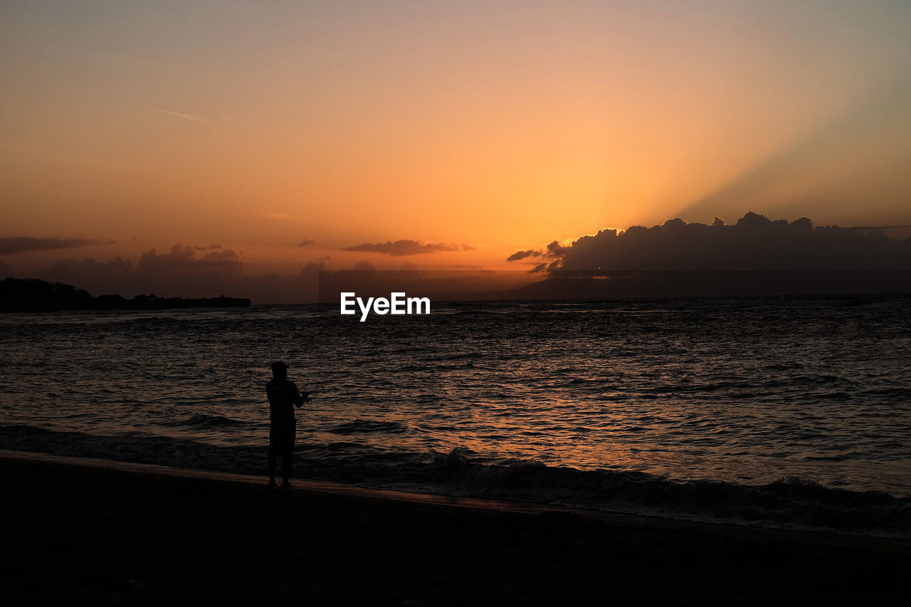 SILHOUETTE PERSON STANDING ON BEACH DURING SUNSET