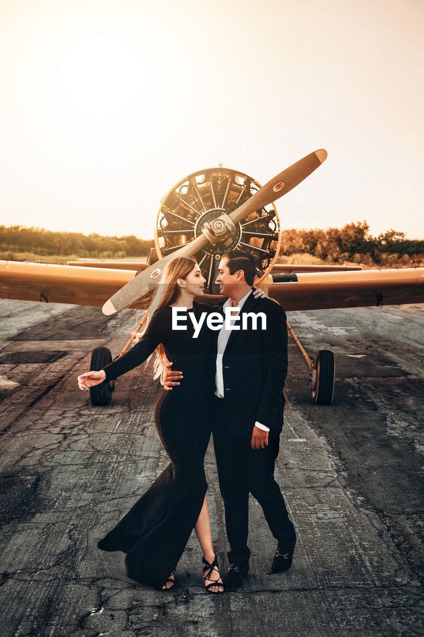 Full length of man with woman standing in airport against sky