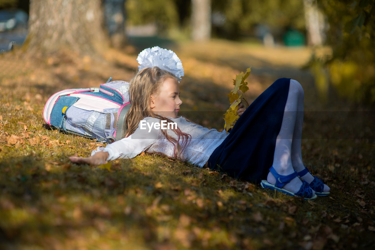 Side view of girl with backpack lying on grassy field in park during autumn