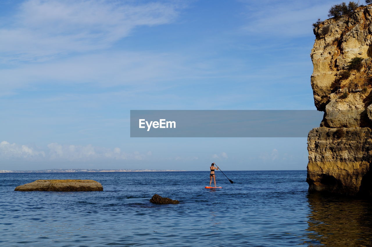 Rear view of woman paddleboarding on sea against sky