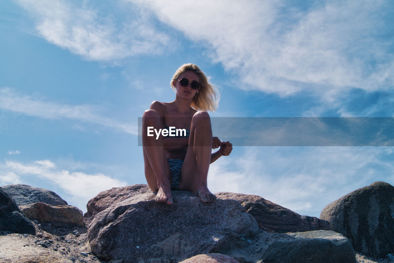 Full length of woman sitting on rock against sky
