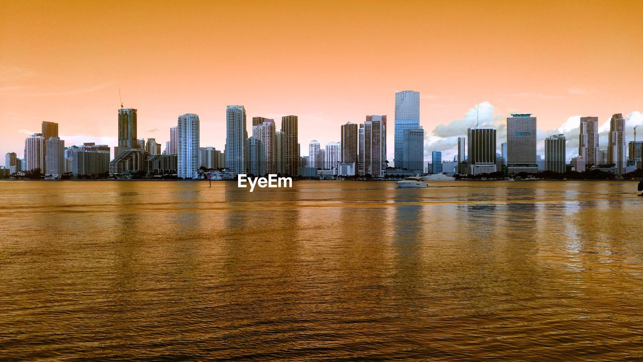 SEA BY BUILDINGS AGAINST SKY DURING SUNSET