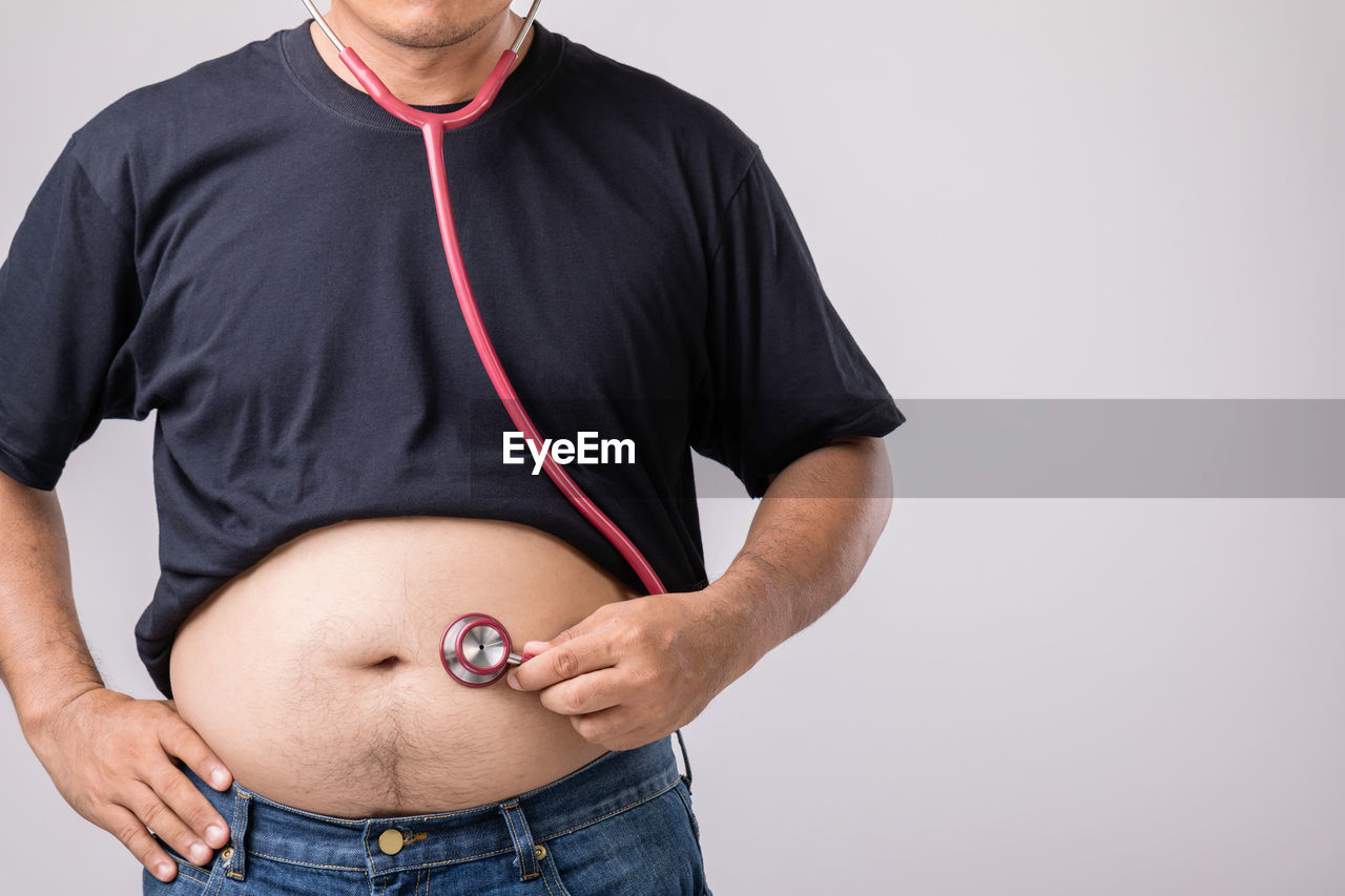 adult, studio shot, one person, men, arm, indoors, clothing, pregnant, casual clothing, standing, midsection, trunk, portrait, lifestyles, front view, parent, anticipation, dieting, sleeve, healthcare and medicine, emotion, vitality, holding, jeans, wellbeing, limb, beginnings, gray, person, positive emotion, hand, waist up, mature adult