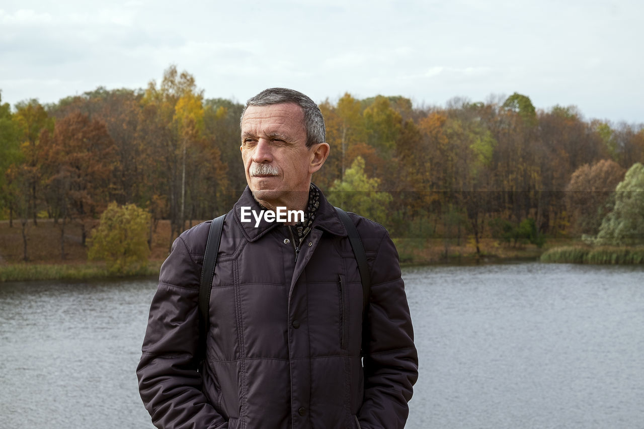 Adult retired man stands by the lake on beautiful autumn day and is resting. slowdown concept. 