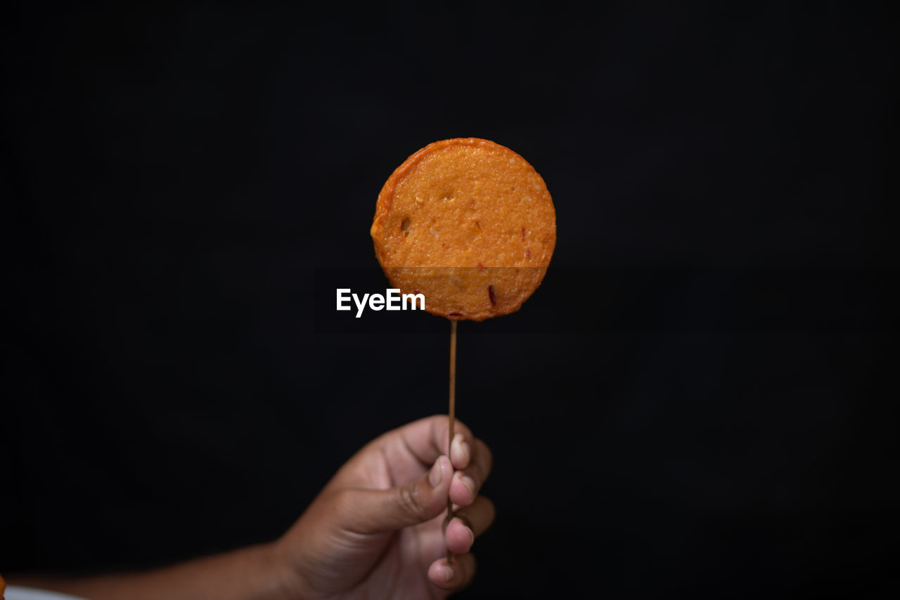 HUMAN HAND HOLDING ICE CREAM AGAINST BLACK BACKGROUND