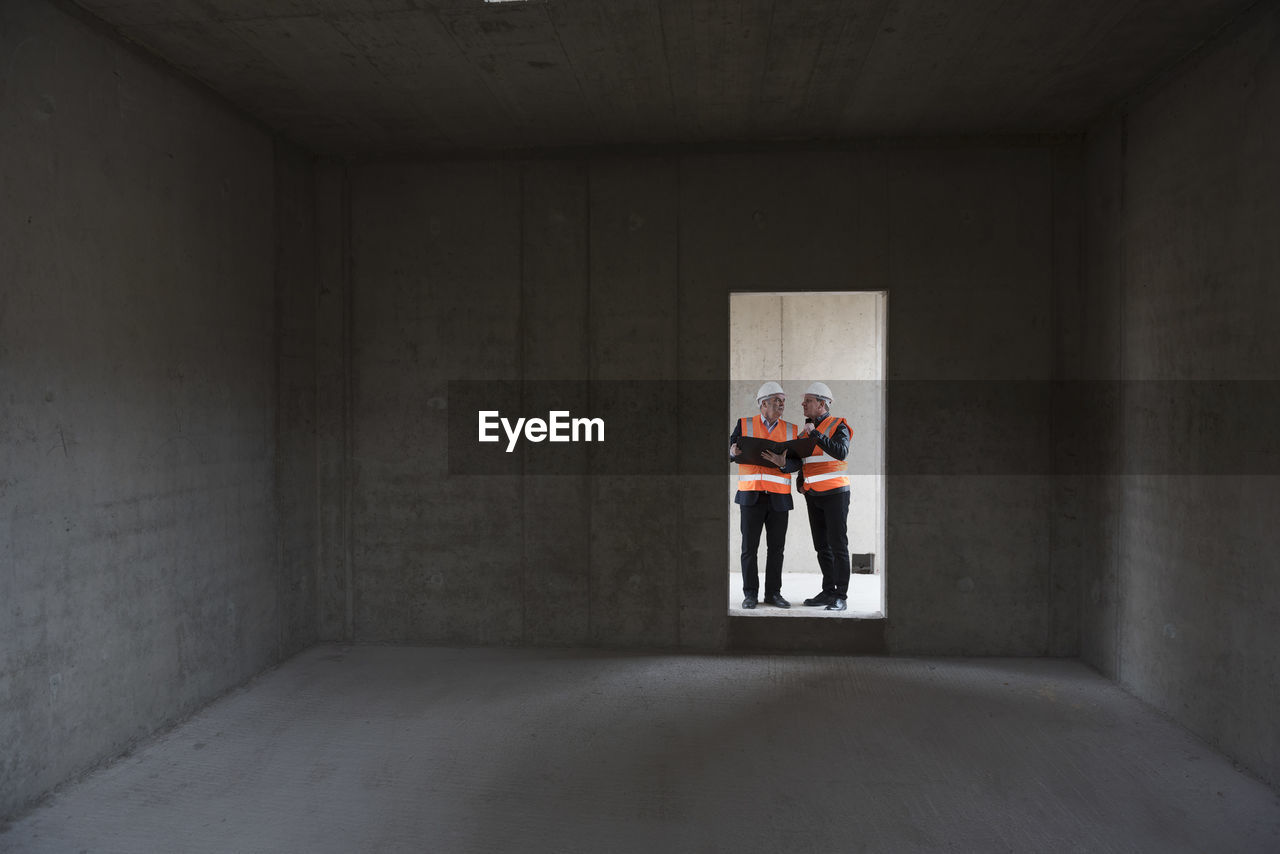 Two men wearing safety vests talking in building under construction