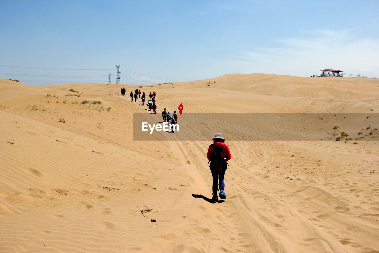 People with flag walking on desert against sky