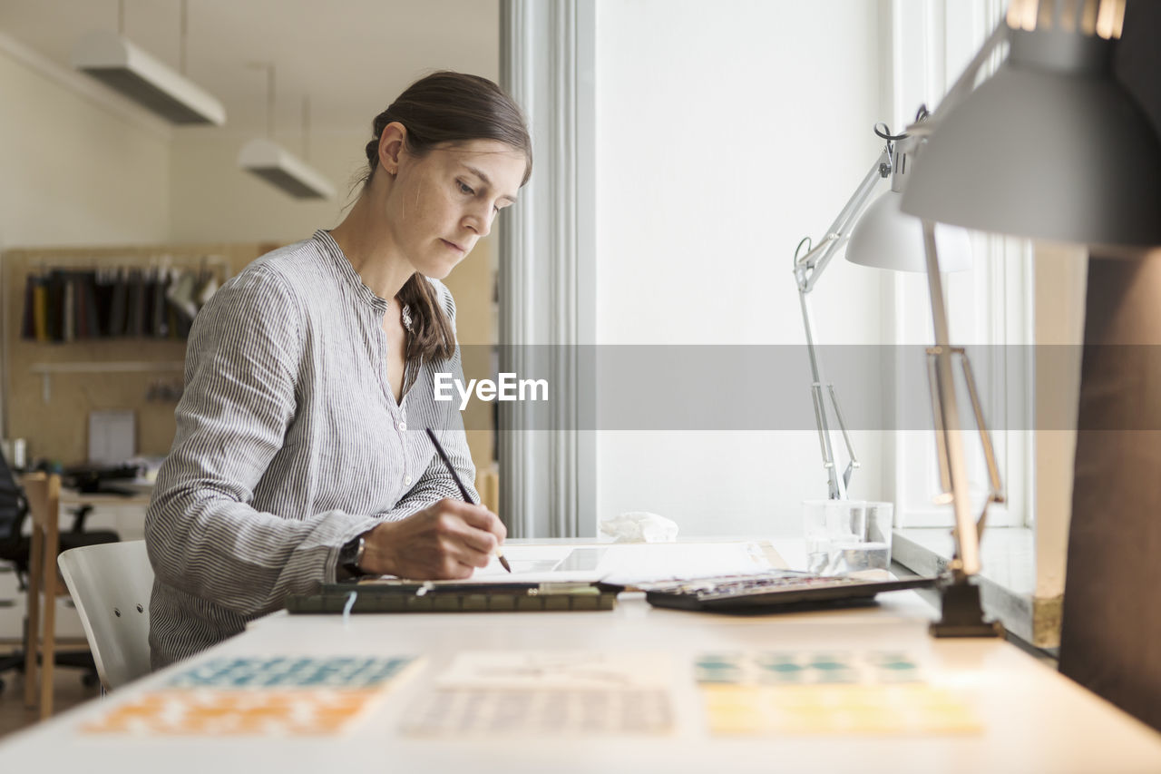 Serious woman painting while sitting at table in creative office