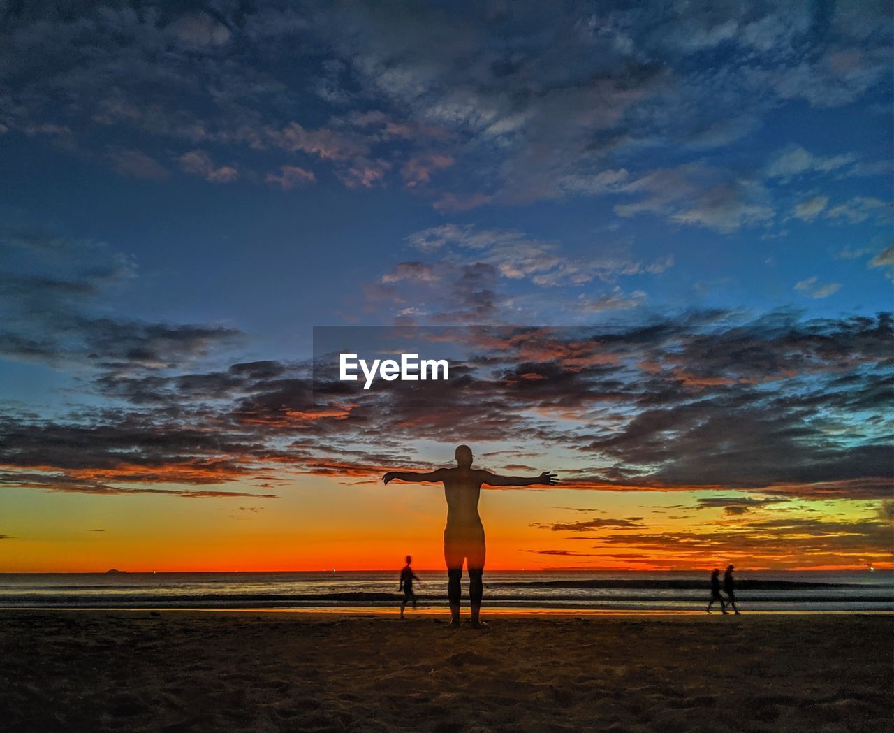 REAR VIEW OF SILHOUETTE MAN STANDING AT BEACH DURING SUNSET