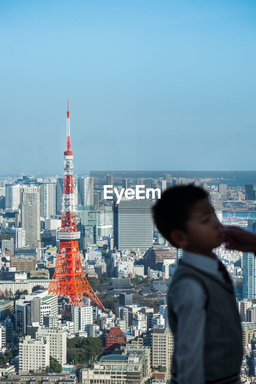 Side view of boy standing against cityscape and sky