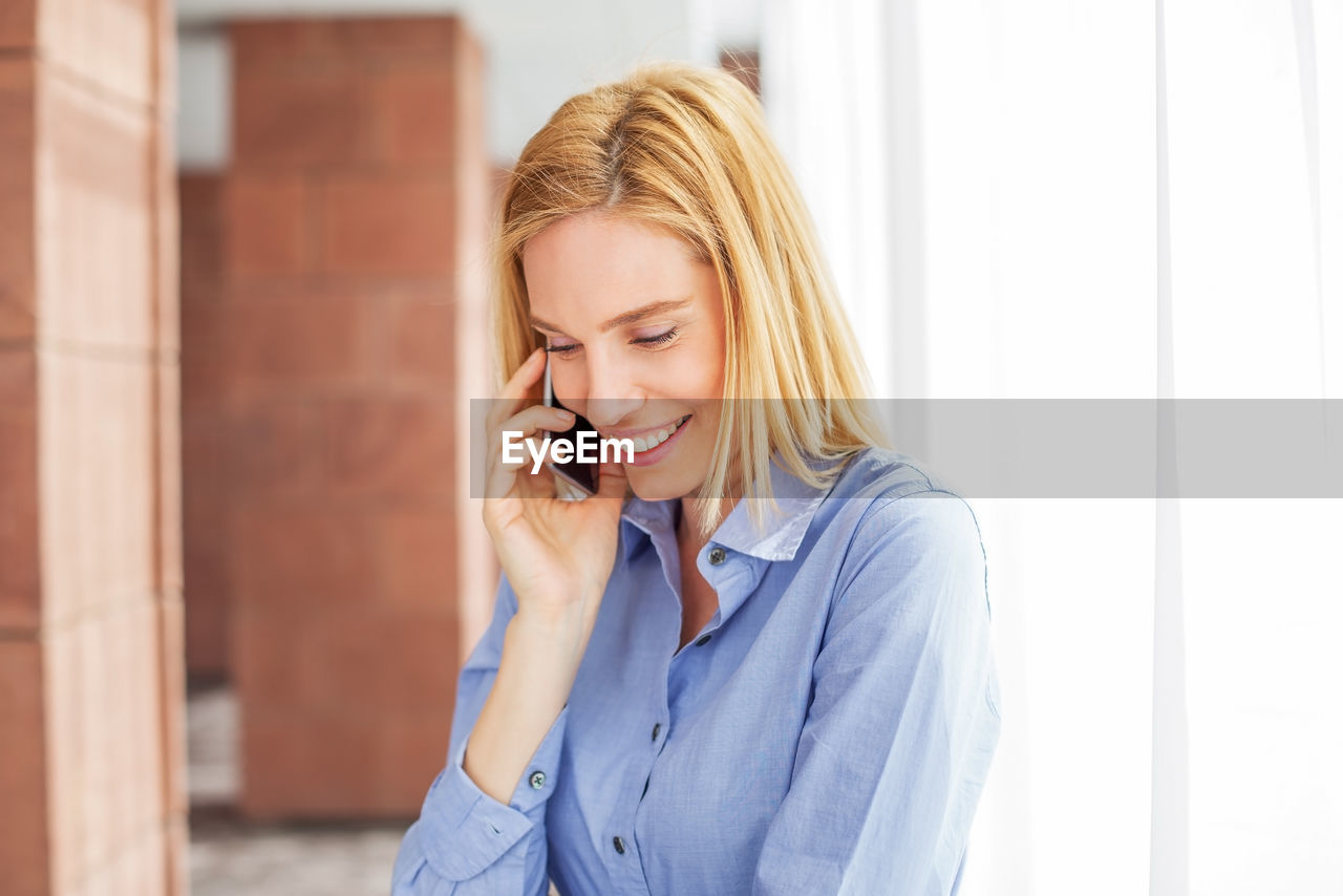 Woman talking on mobile phone while standing against wall