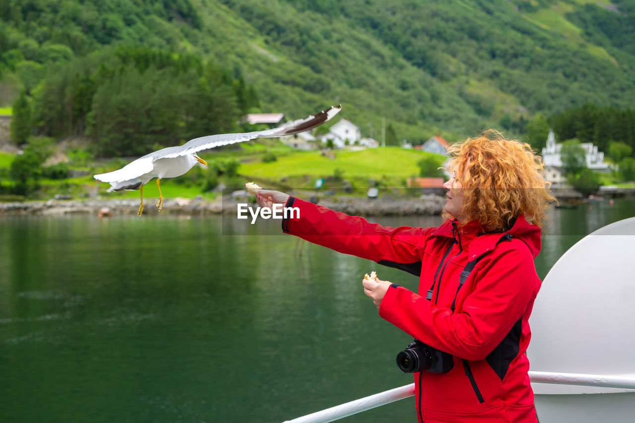 rear view of young woman with arms outstretched standing against lake