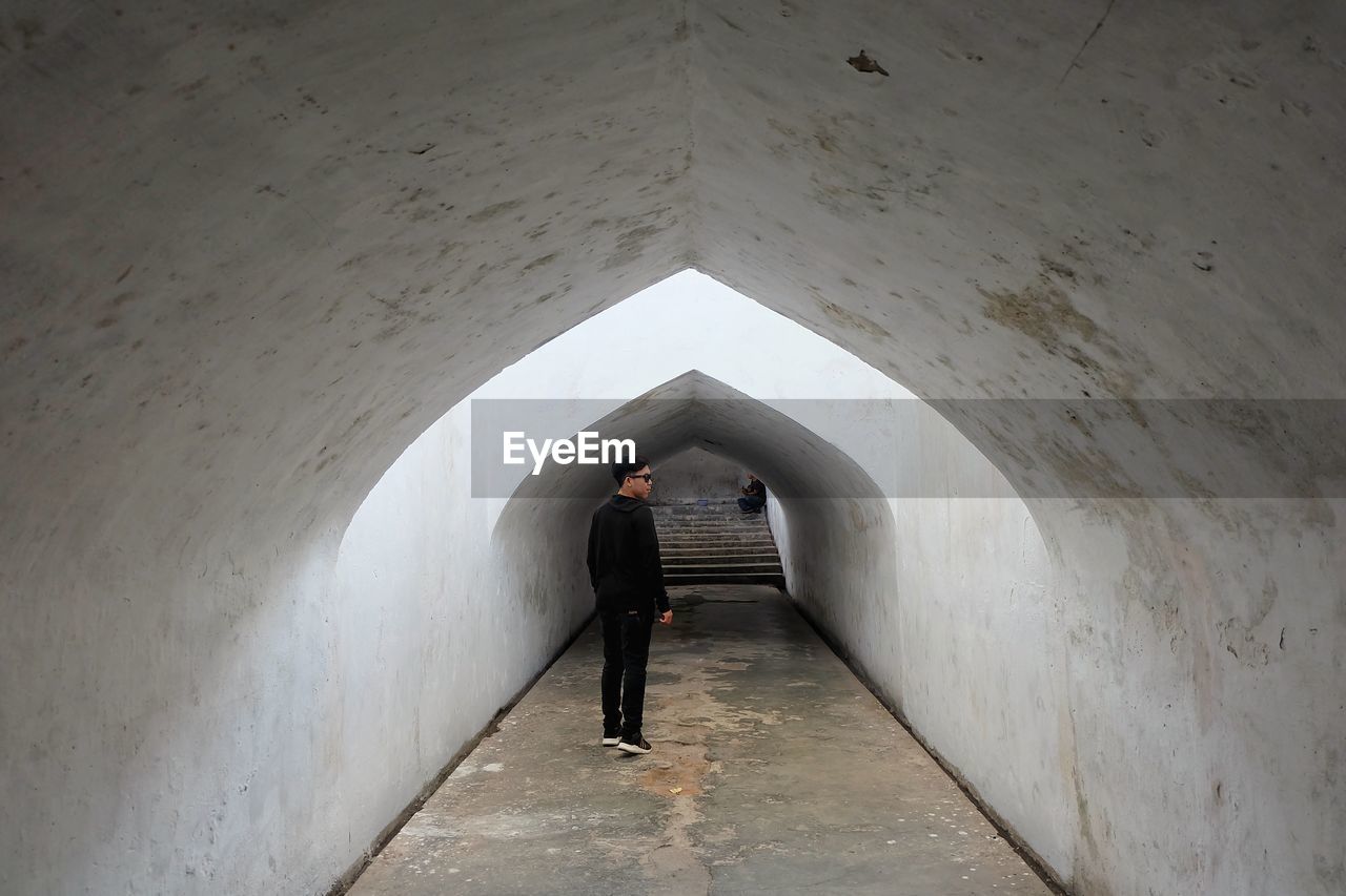 MAN STANDING IN CORRIDOR OF BUILDING