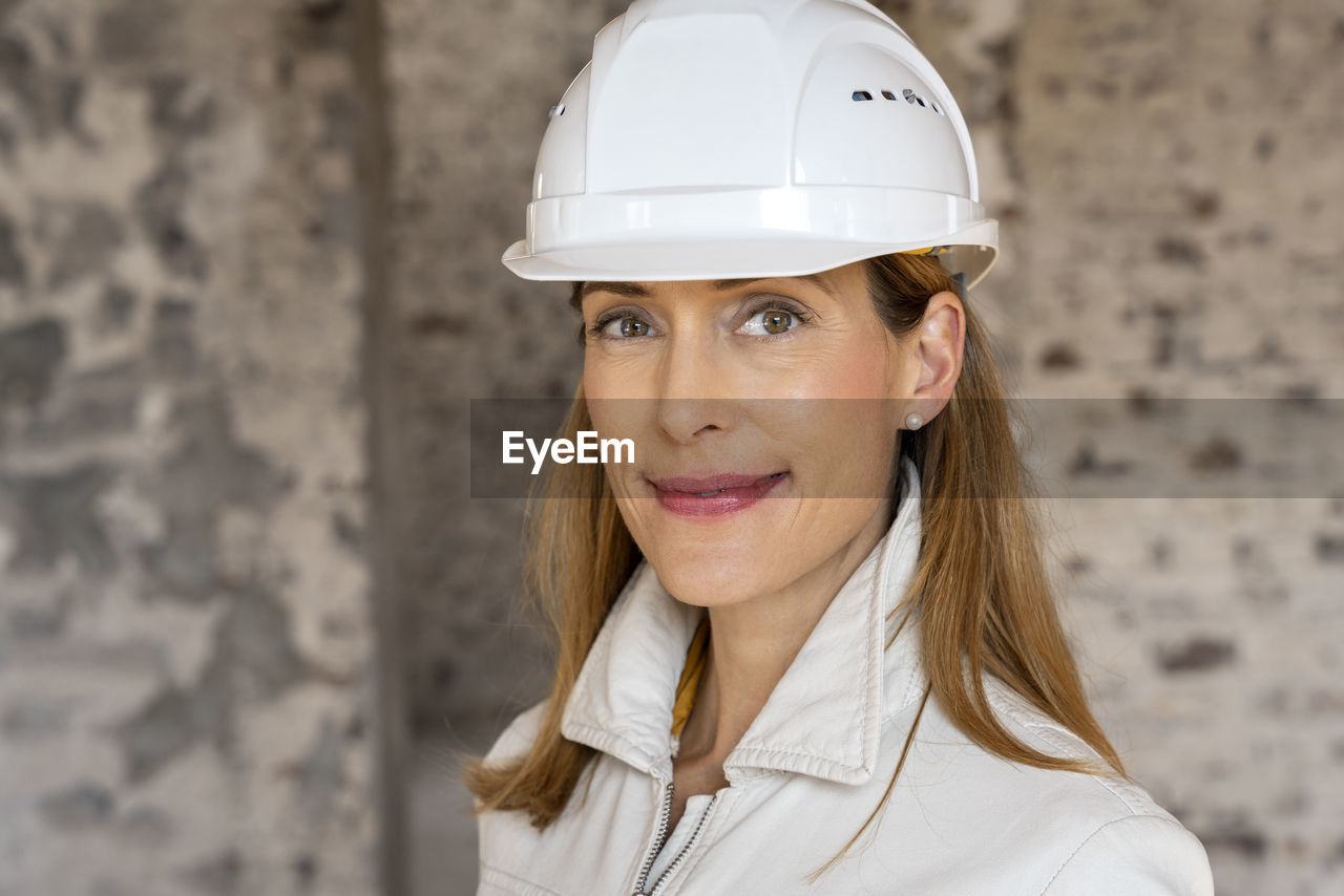 Businesswoman wearing hardhat smiling while standing at construction site