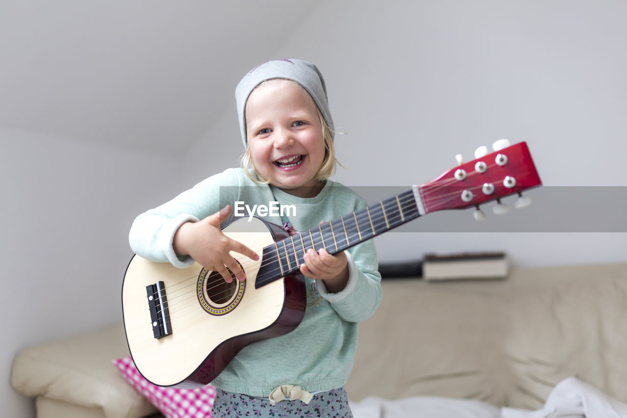 Portrait of happy girl playing guitar at home