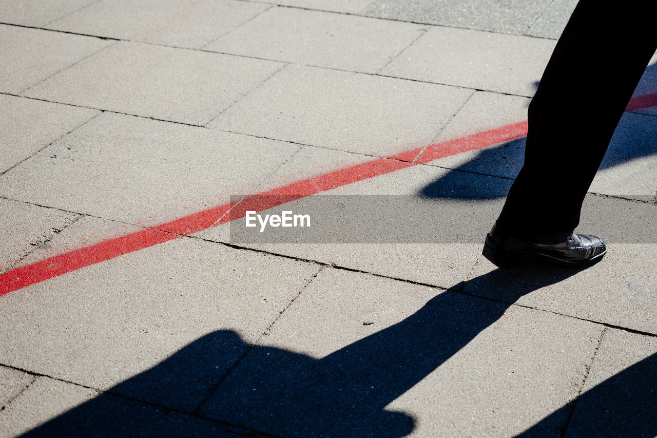 Low section of man walking on footpath during sunny day