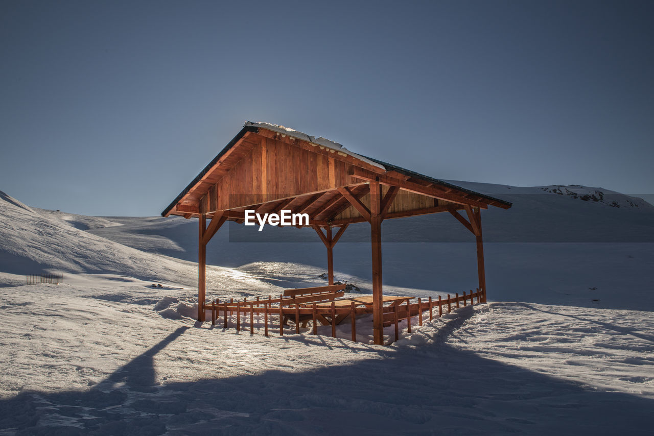 Gazebo on snow covered land against clear sky