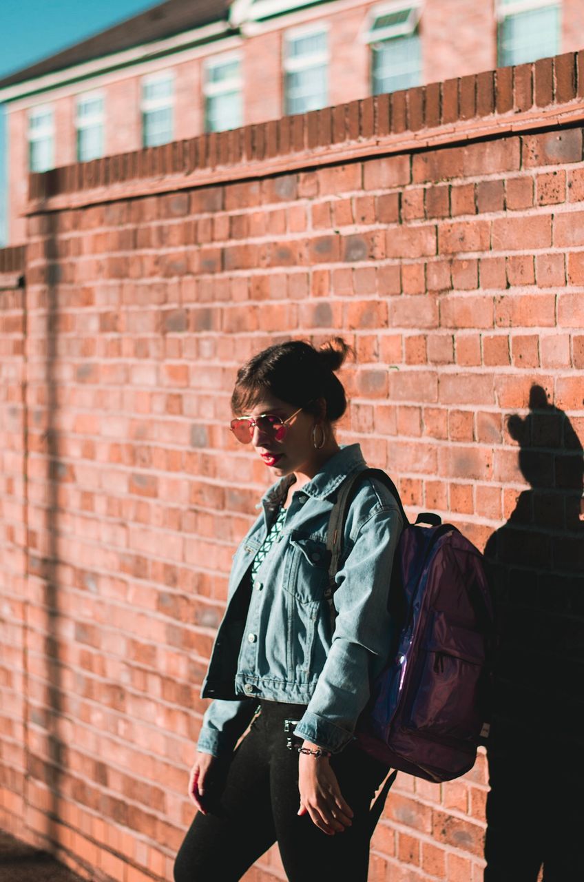 Young woman carrying backpack while standing by brick wall