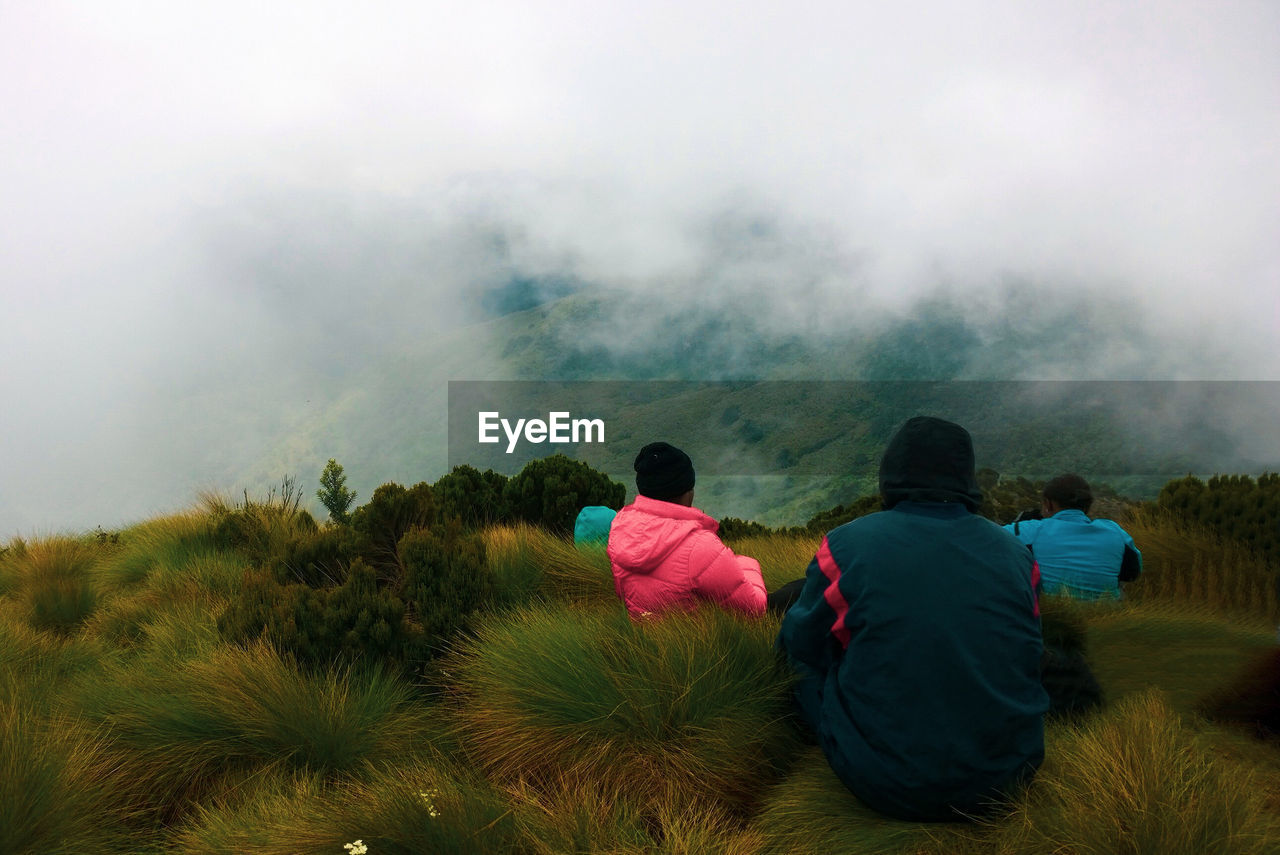 Rear view of people sitting on mount top  against foggy mountain 